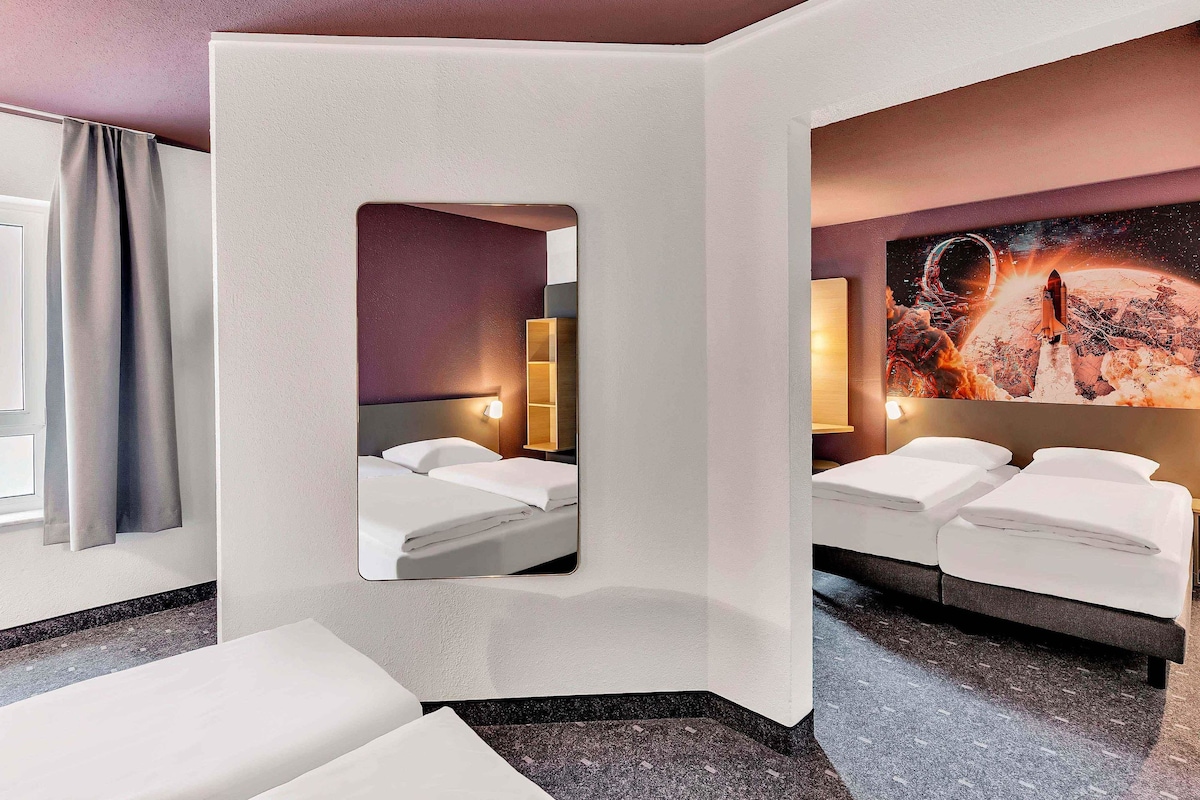 Una habitación de hotel moderna con dos camas, un espejo grande y una obra de arte con temática espacial.