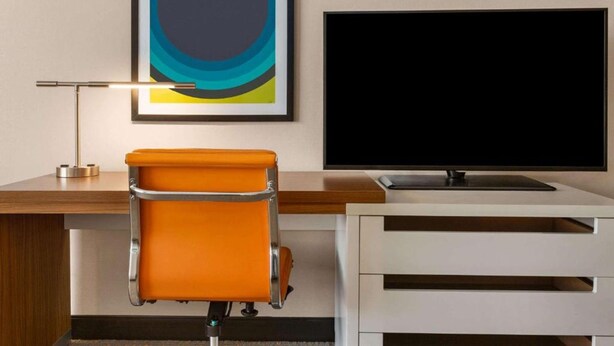 Habitación de hotel con escritorio, una silla, televisión de pantalla plana y un cuadro abstracto enmarcado.