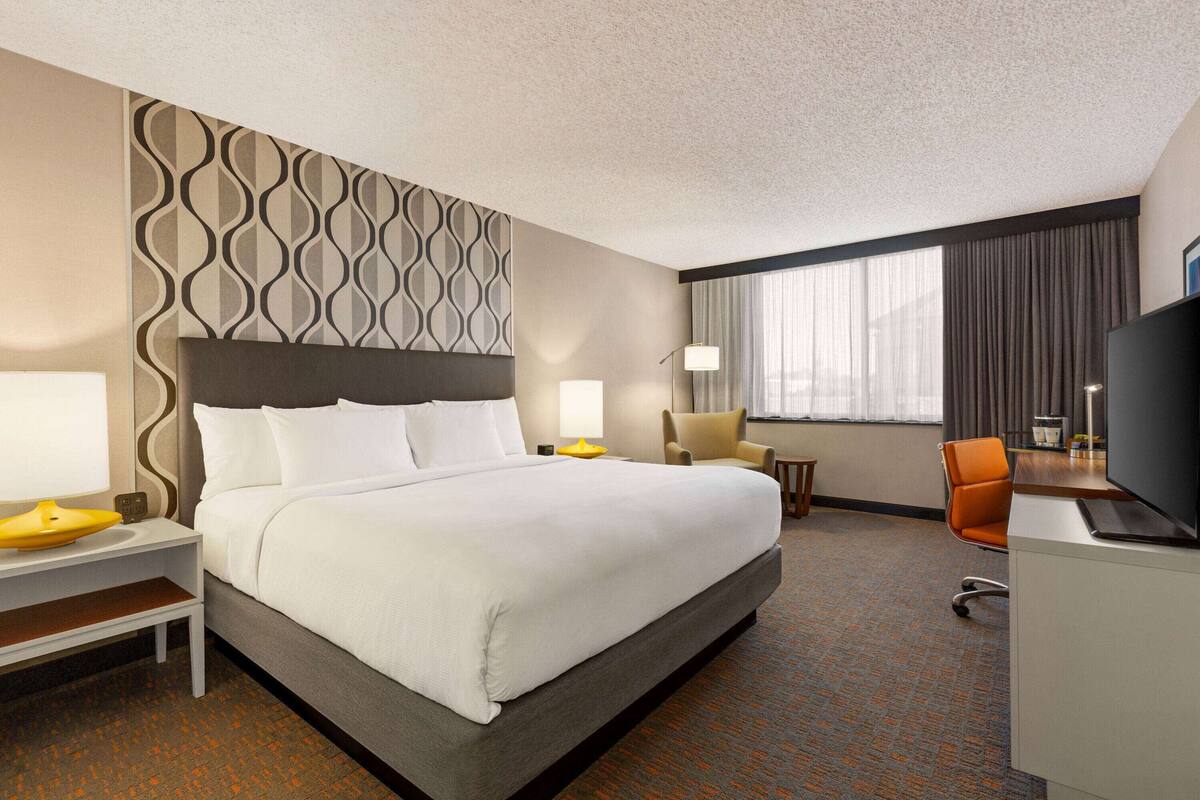 Een hotelkamer met een groot bed, een bureau met een flatscreen televisie, een stoel en een bureaulamp.