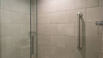 A modern bathroom with a glass-enclosed shower, a white bathtub, and beige tiles.