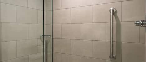 Un baño moderno con ducha envuelta en vidrio, una bañera blanca y baldosas color beige.