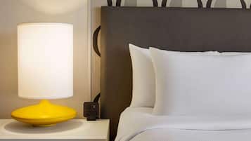 A neatly made bed with white bedding, a modern yellow lamp on a white nightstand, and a power outlet.
