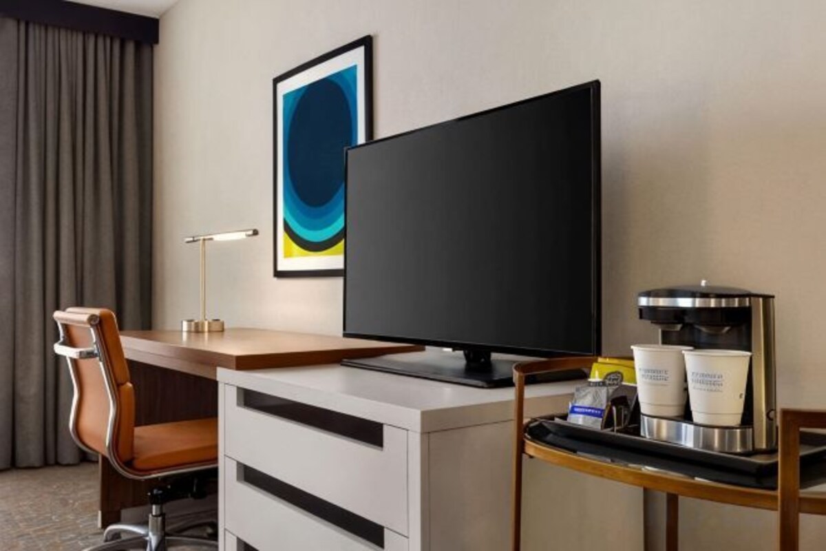 Una habitación de hotel con escritorio, televisión, cafetera y una silla.