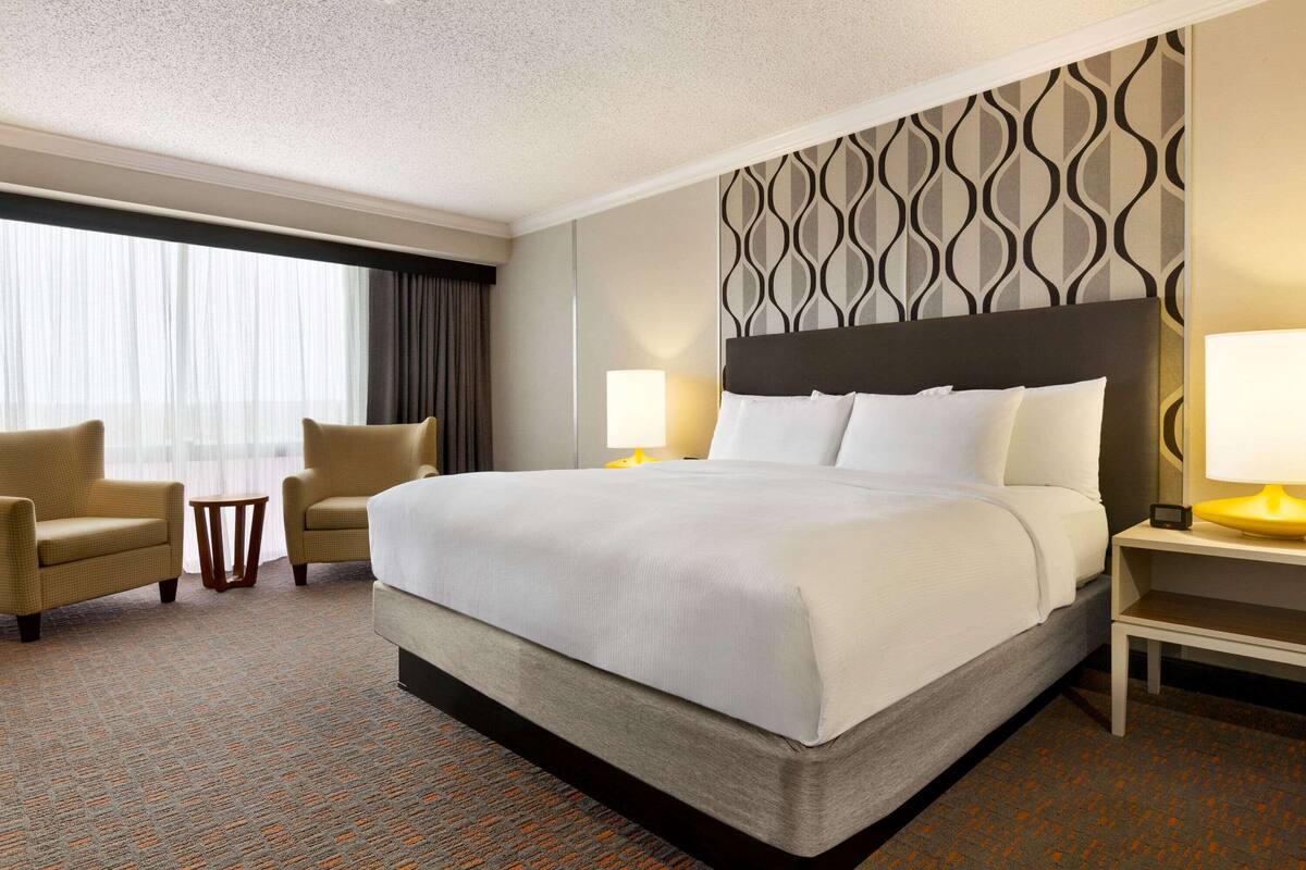 Een hotelkamer met een groot bed, twee fauteuils, een klein bijzettafeltje en een nachtkastje met een lamp.