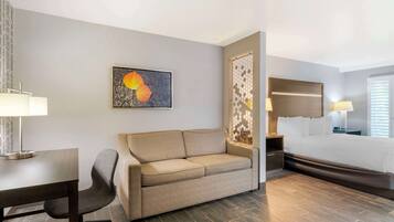 A hotel room with a sofa, a desk, a bed, and a wall-mounted artwork.