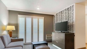 A modern living room with a sofa, a small table, a TV on a cabinet, and a decorative wall panel. - Best Western Corvallis (Corvallis)