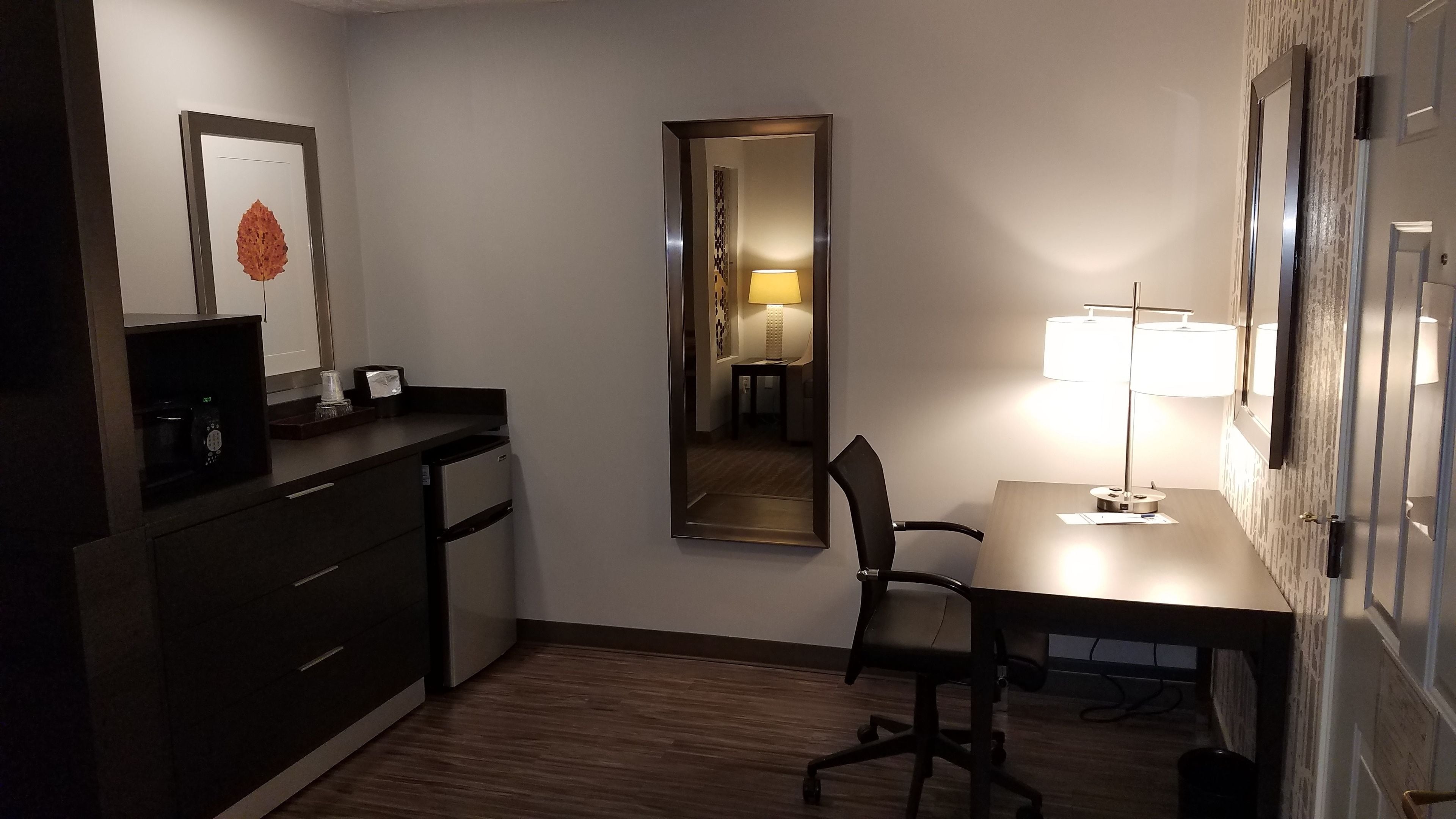 A compact hotel room with a desk, chair, and a small kitchenette area.