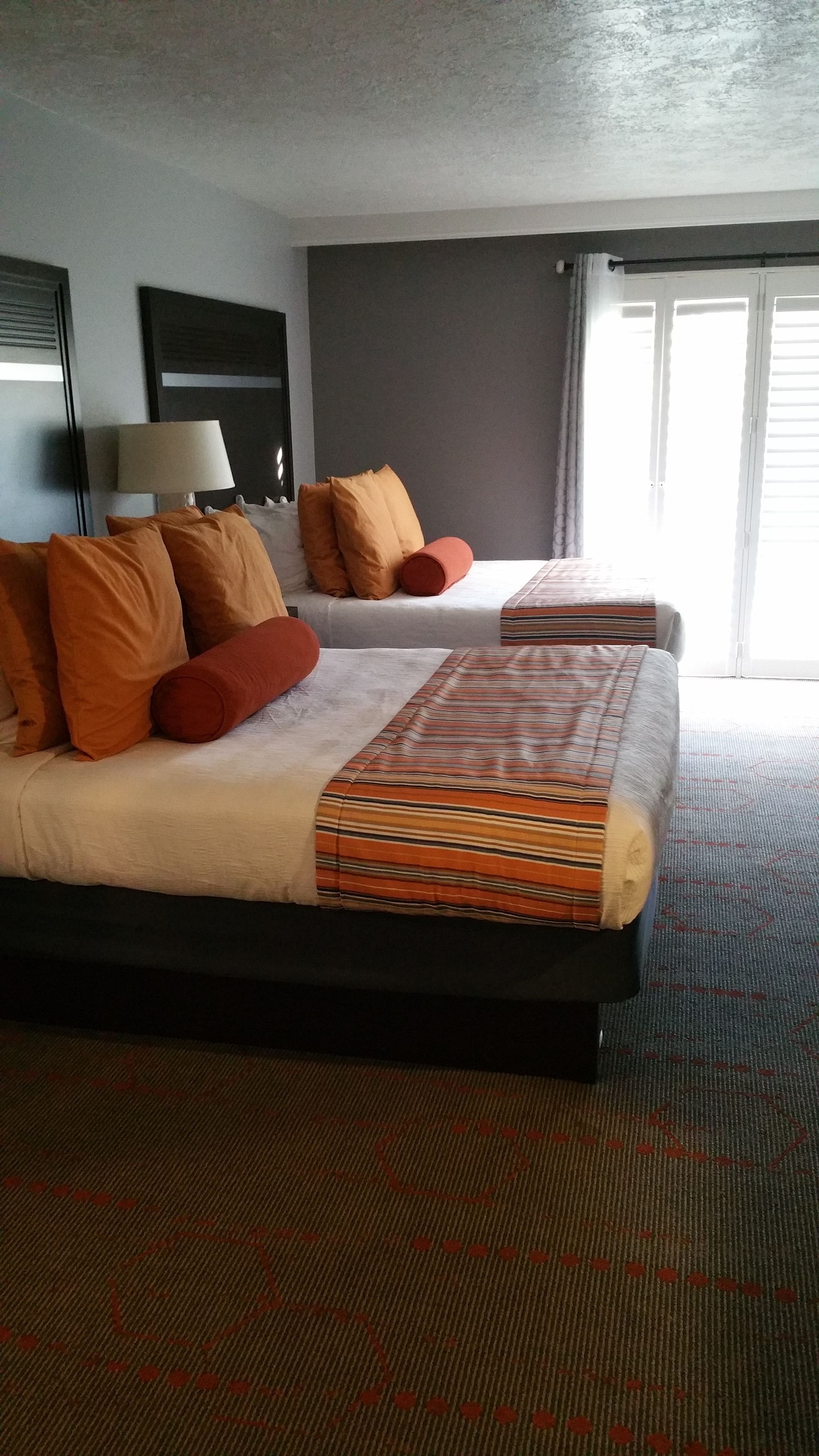 A hotel room with a large bed, two pillows, a striped blanket, a lamp, and a window with curtains.