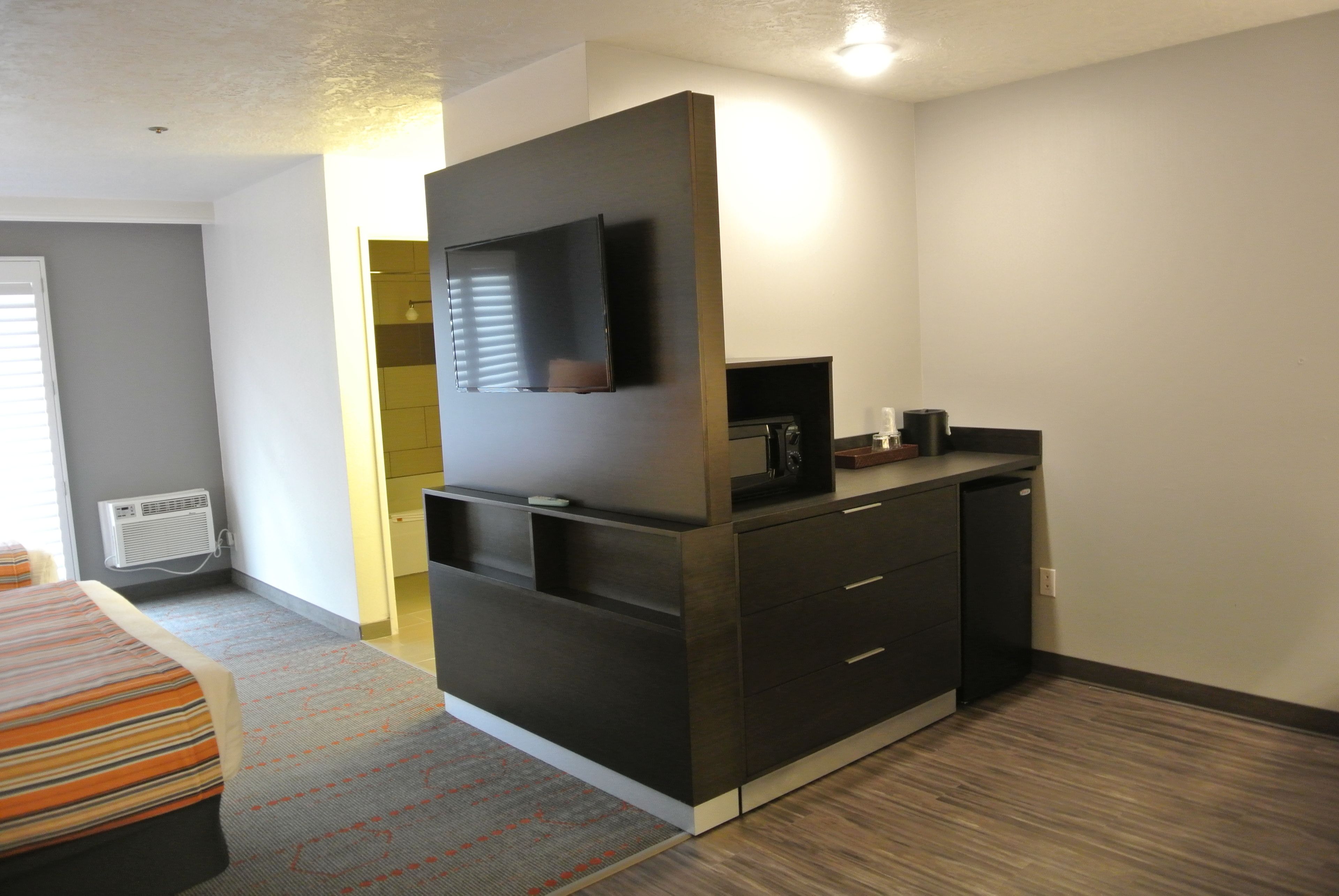 Habitación de hotel con cama, televisión de pantalla plana montada en un mueble oscuro, microondas y cafetera pequeña.