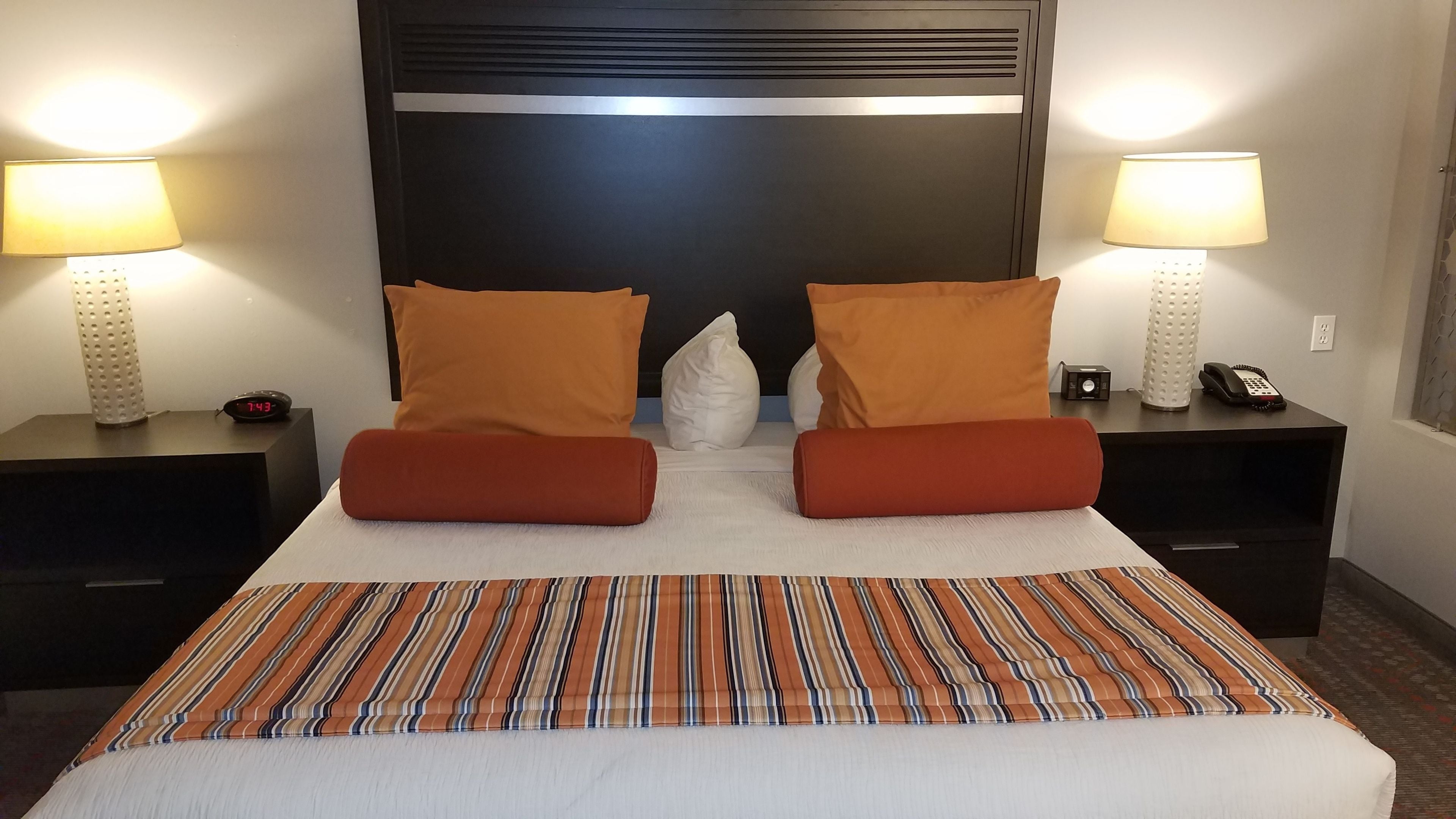 Een hotelkamer met een groot bed, twee nachtkastjes, een digitale klok, een telefoon en twee lampen.
