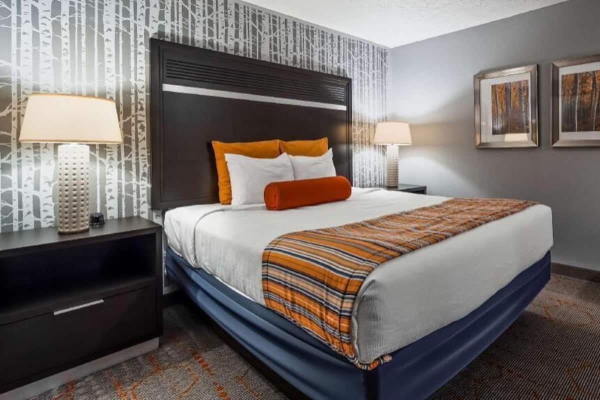 Una habitación de hotel con cama, mesitas de noche, lámpara y cuadros en la pared.