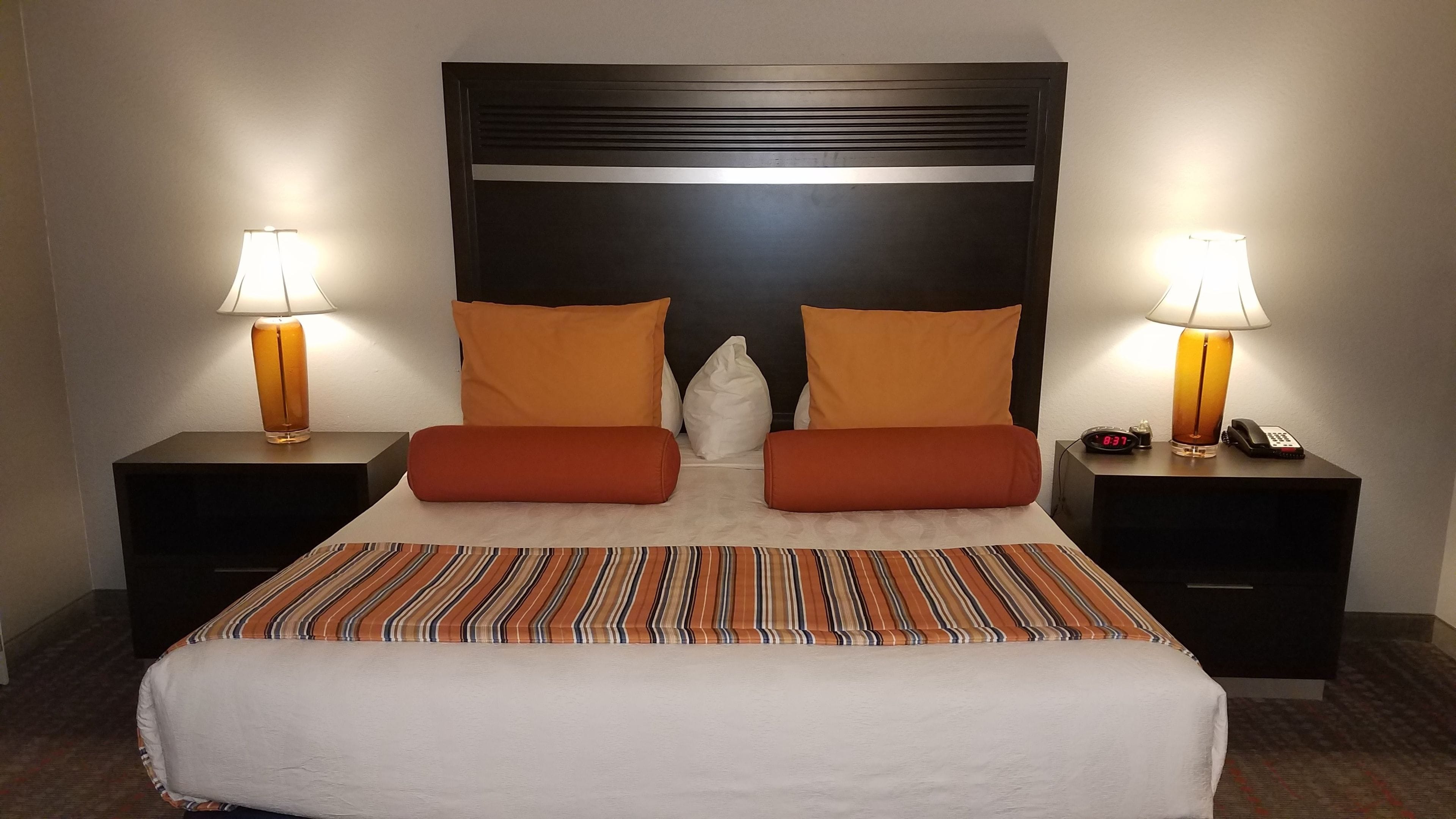 A hotel room with a large bed, two nightstands, a headboard, and two lamps.