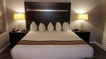 A hotel room with a large bed, two bedside tables with lamps, a clock, and a phone on one of the tables.