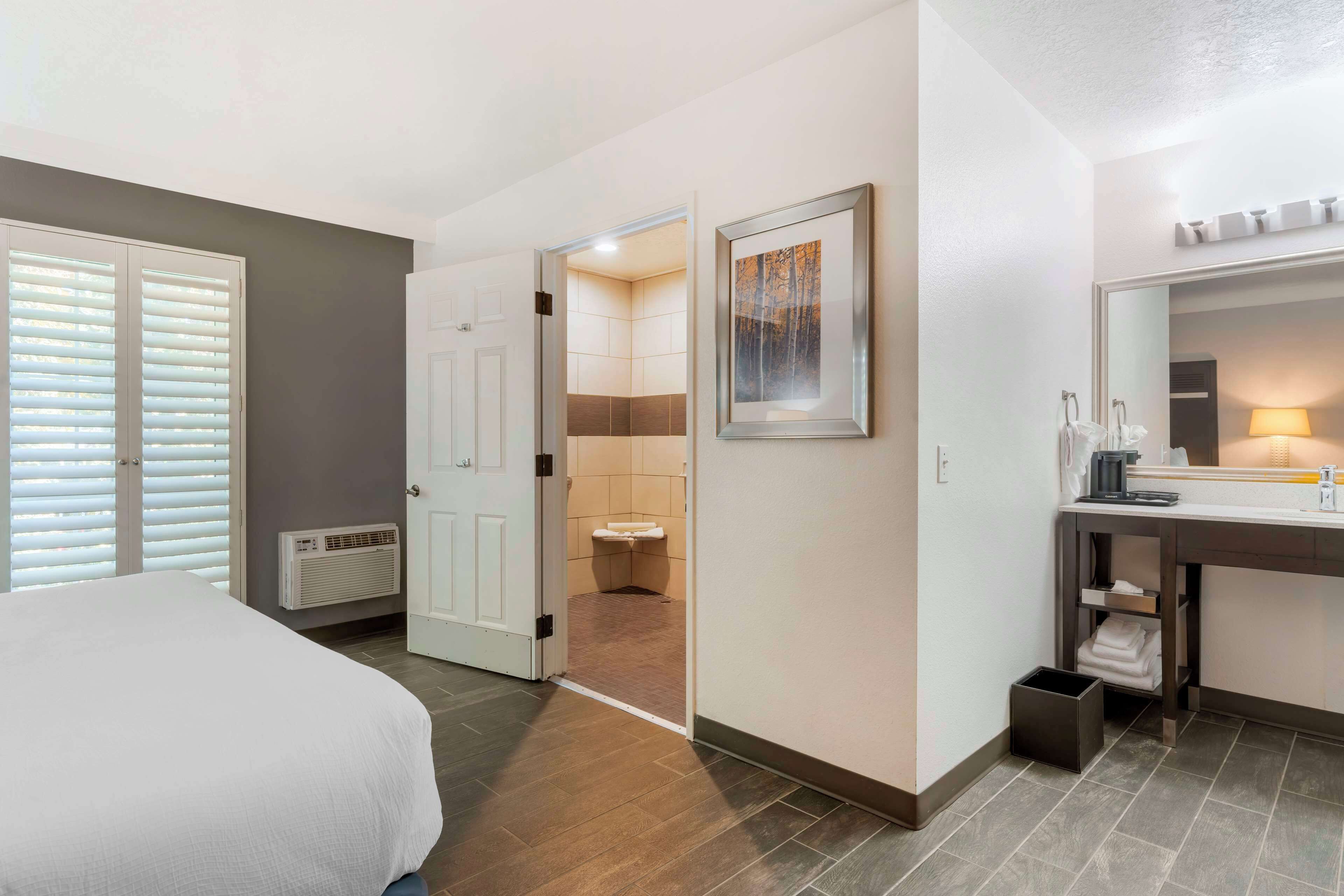 A hotel room with a bed, a bathroom with a sink and mirror, and a door leading to another room.
