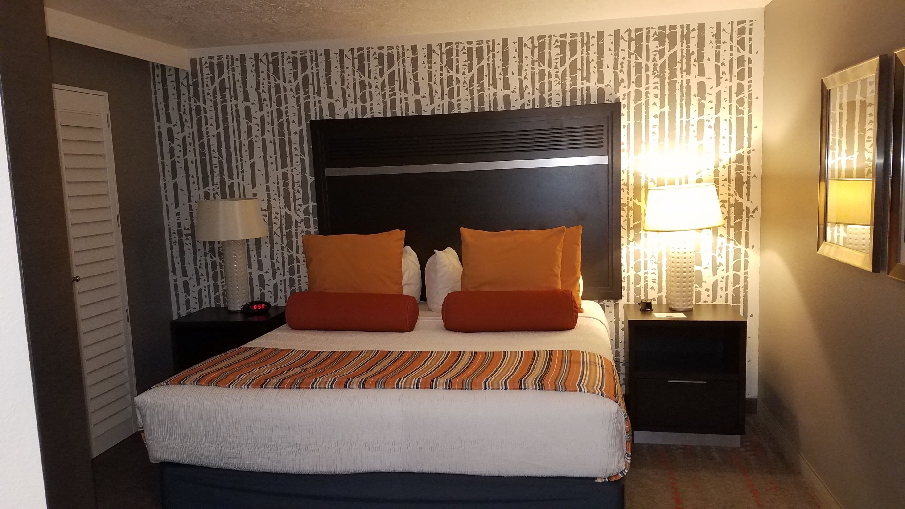 A hotel room with a large bed, two nightstands, a wall clock, and patterned wallpaper.