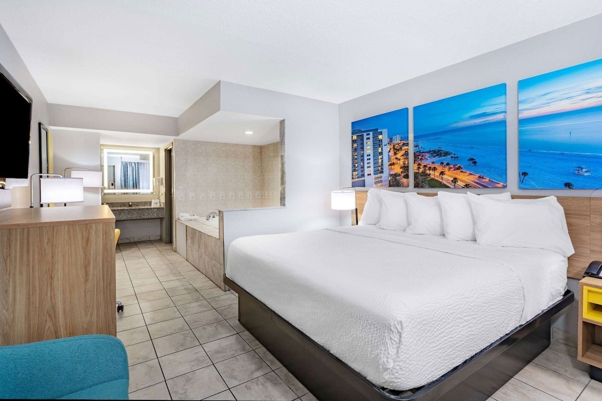 Ein Hotelzimmer mit einem großen Bett, einem Schreibtisch, einem Stuhl, einem Badezimmer und Kunstwerken an den Wänden.