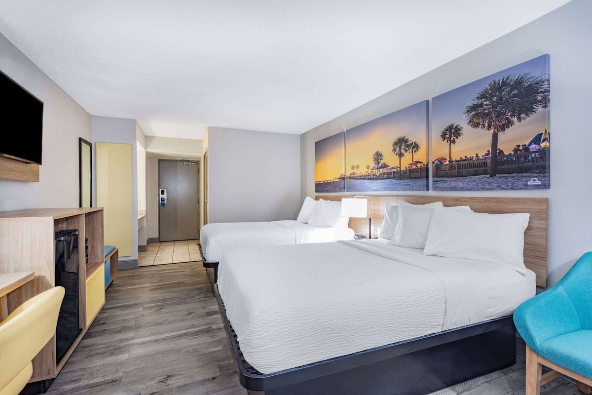 Ein Hotelzimmer mit zwei Betten, einem Schreibtisch, einem Stuhl und einem Bild mit einer Strandansicht.