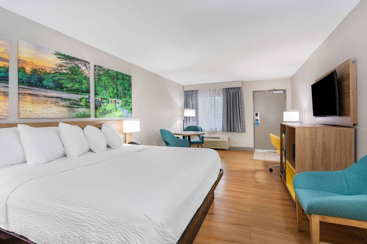 Ein Hotelzimmer mit einem großen Bett, einem Schreibtisch mit Stuhl, einem Fernseher und einem Fenster mit Vorhängen.