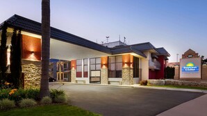 A Days Inn & Suites hotel with a modern design, featuring a stone facade, large windows, and a well-lit entrance. - Days Inn & Suites by Wyndham Anaheim At Disneyland Park (Anaheim)