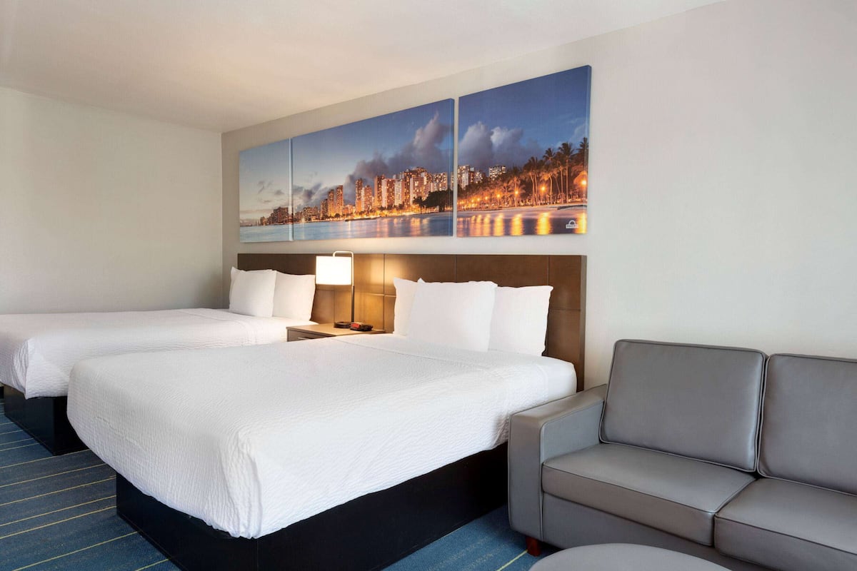 A hotel room with two beds, a sofa, and a cityscape painting on the wall.