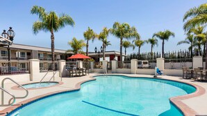 A swimming pool with a tiled edge, surrounded by palm trees and a building with balconies. - Days Inn & Suites by Wyndham Anaheim At Disneyland Park (Anaheim)