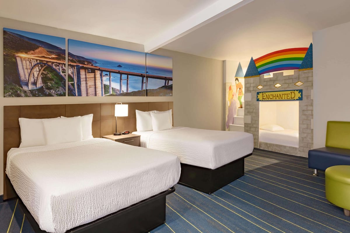 A hotel room with two beds, a nightstand, a lamp, and a bathroom with a rainbow-themed wall.