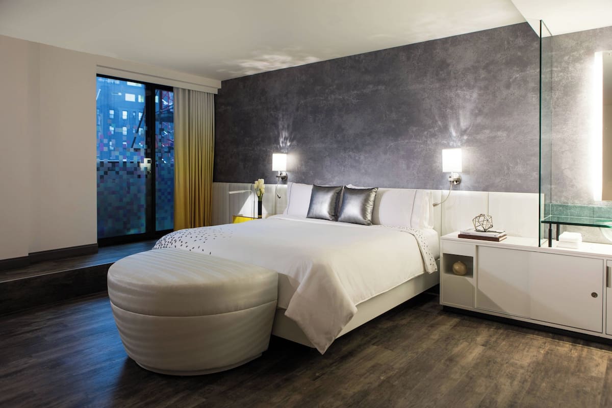 Habitación de hotel moderna con una cama grande, cabina de ducha de vidrio y vista nocturna de la ciudad.