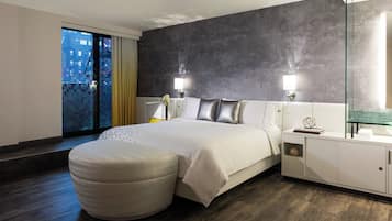 A modern hotel room with a large bed, a glass shower enclosure, and a view of the city at night.