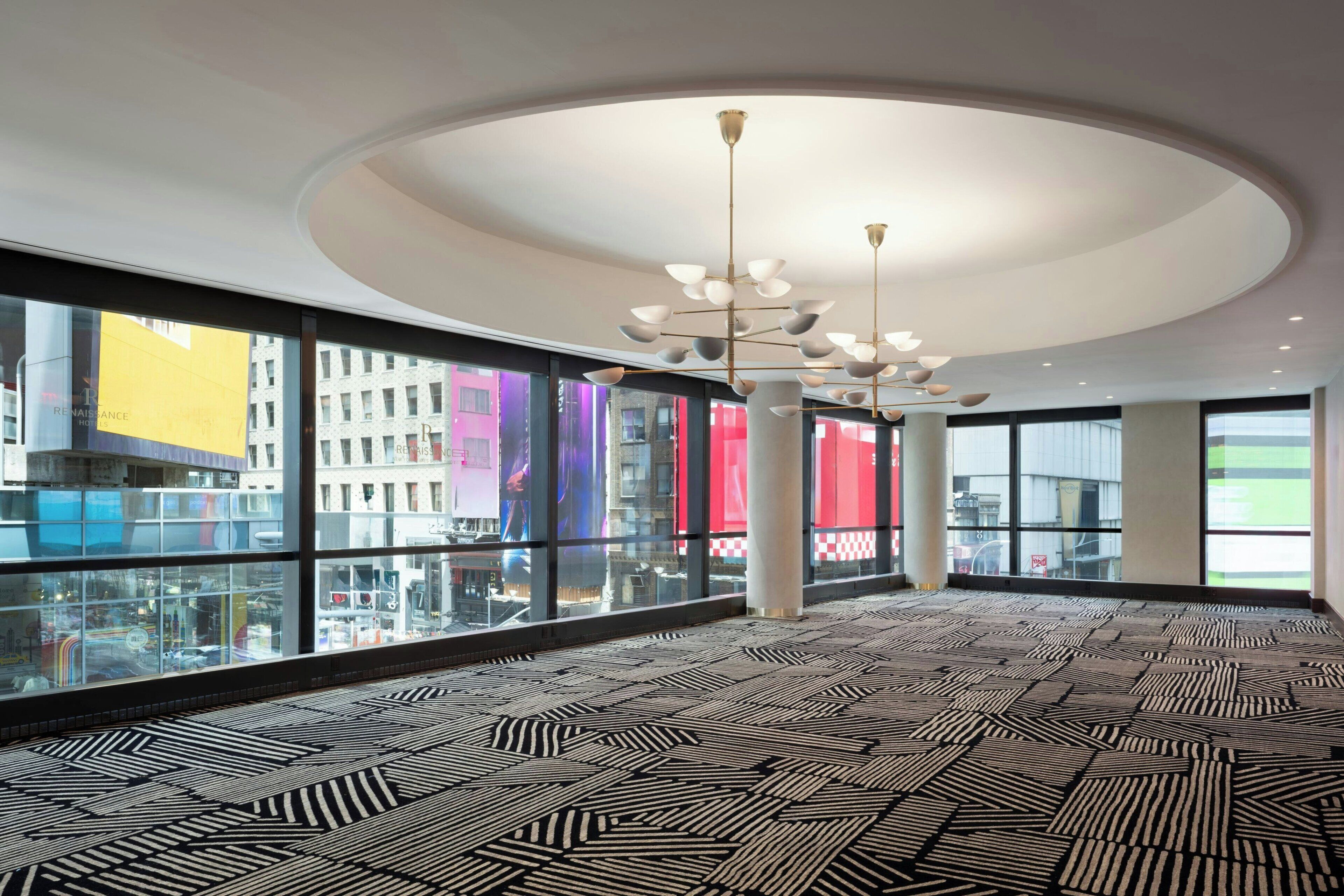 A spacious hotel lobby with a patterned floor, large windows, and a modern chandelier.