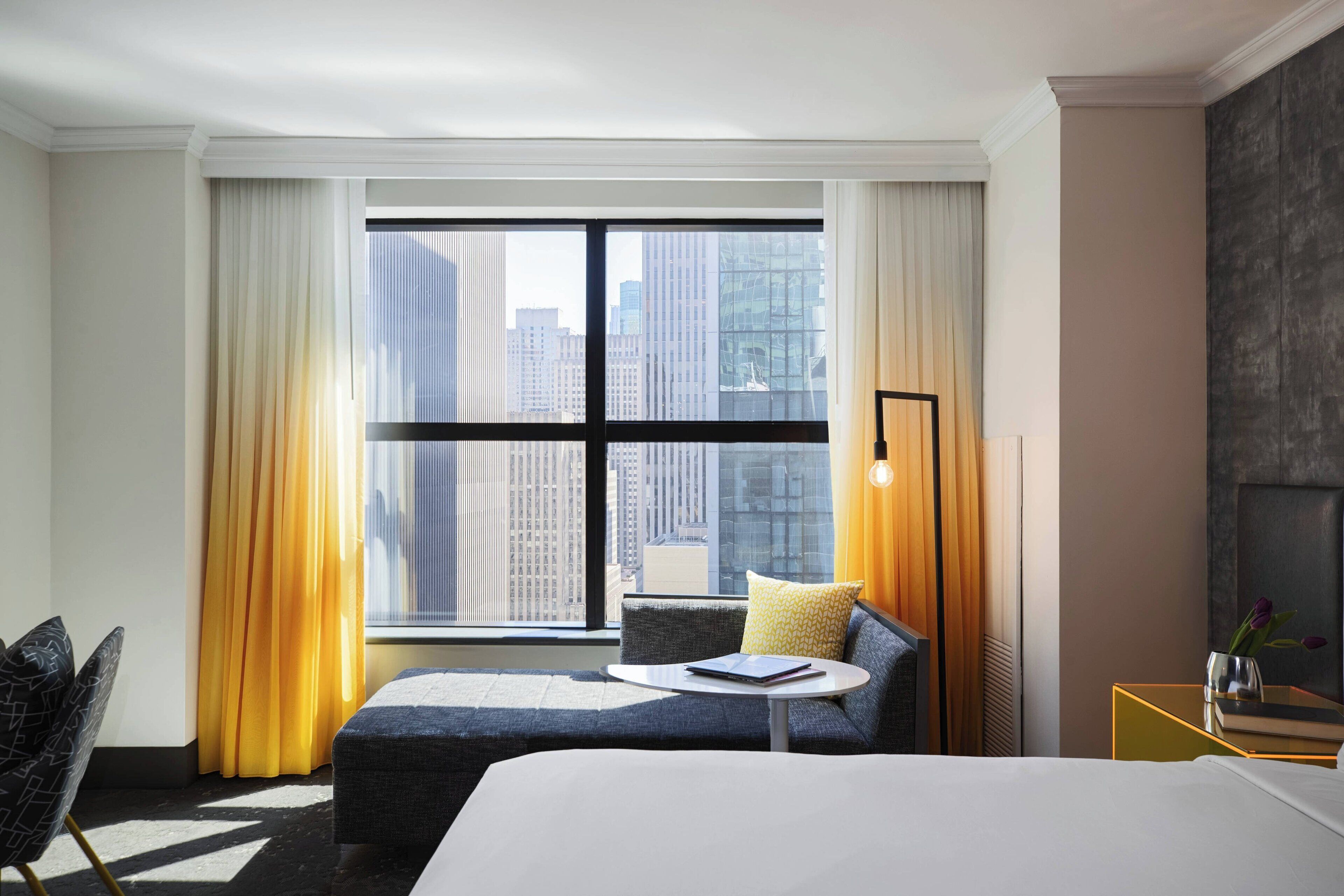 Una habitación de hotel moderna con un ventanal grande, un sofá, una mesita y una cama.