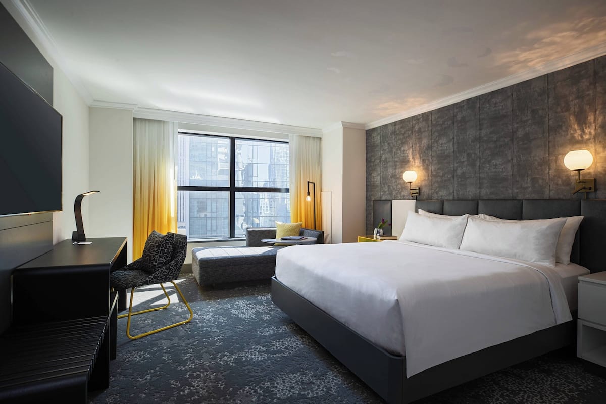 Habitación de hotel moderna con una cama grande, un escritorio, una silla y vistas a la ciudad desde la ventana.