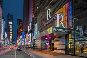 A brightly lit urban street with storefronts, including a Renaissance hotel. - Renaissance New York Times Square Hotel by Marriott (New York)