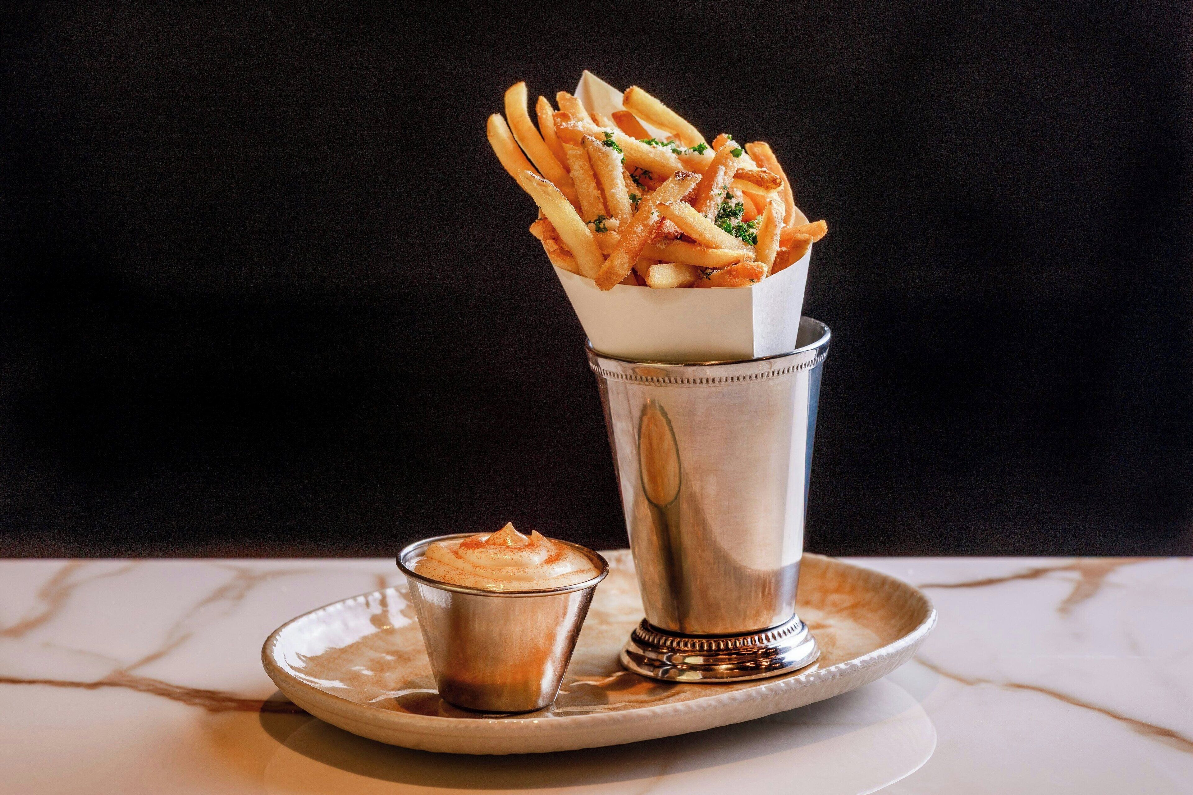 A tray with a glass of a beverage, a small cup of sauce, and a container of fries.