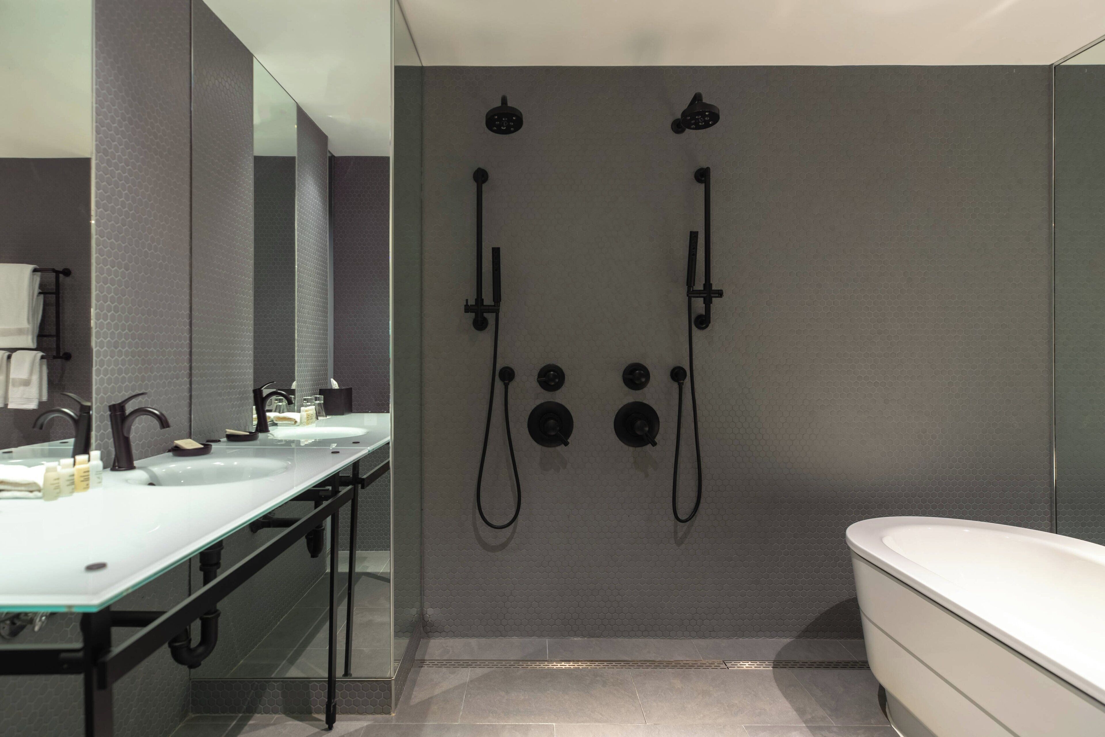 A modern bathroom with a glass shower enclosure, a large bathtub, and a vanity with a mirror and two sinks.