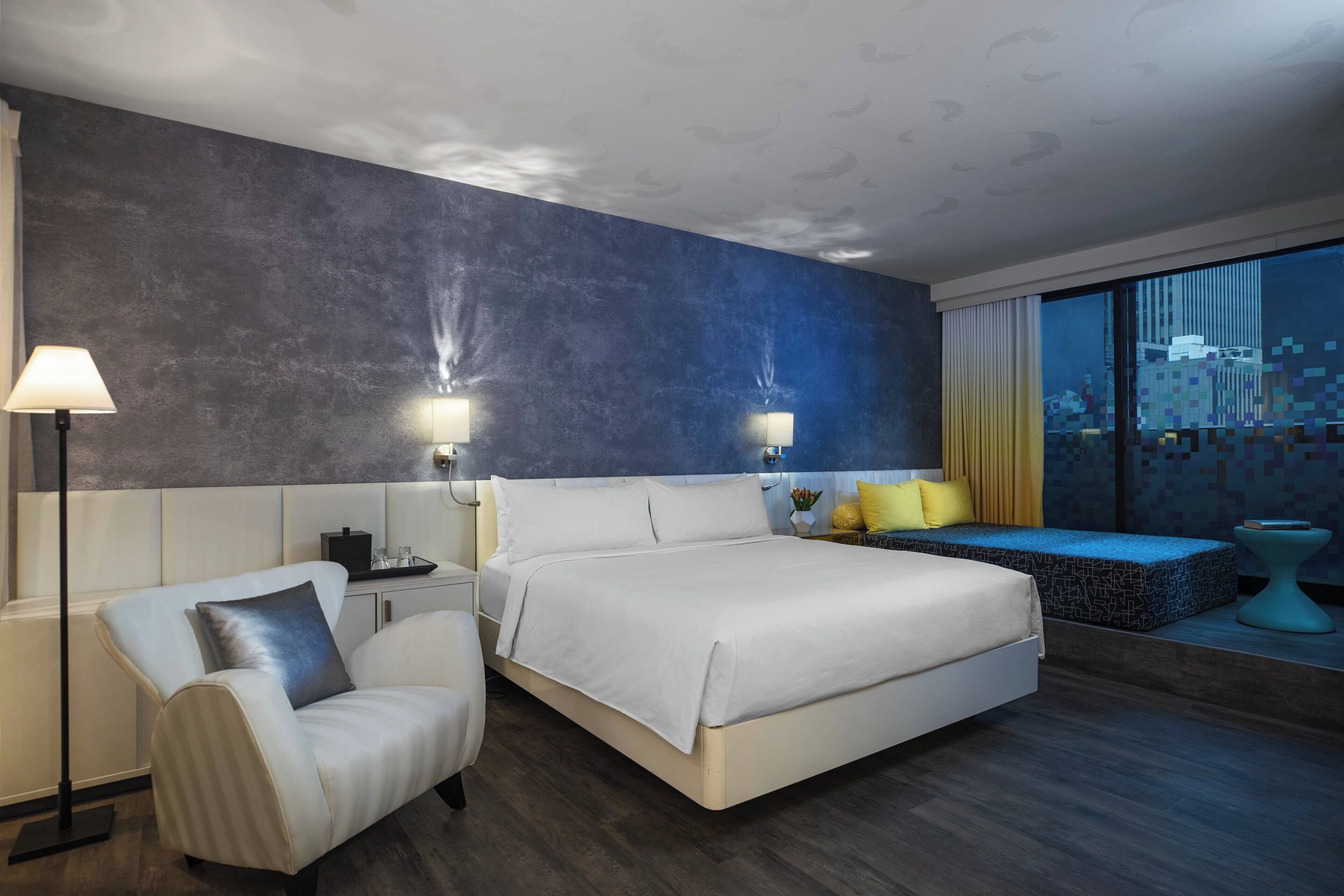 Ein modernes Hotelzimmer mit einem großen Bett, einer Sitzecke mit Blick und einem Schreibtisch mit Lampe.