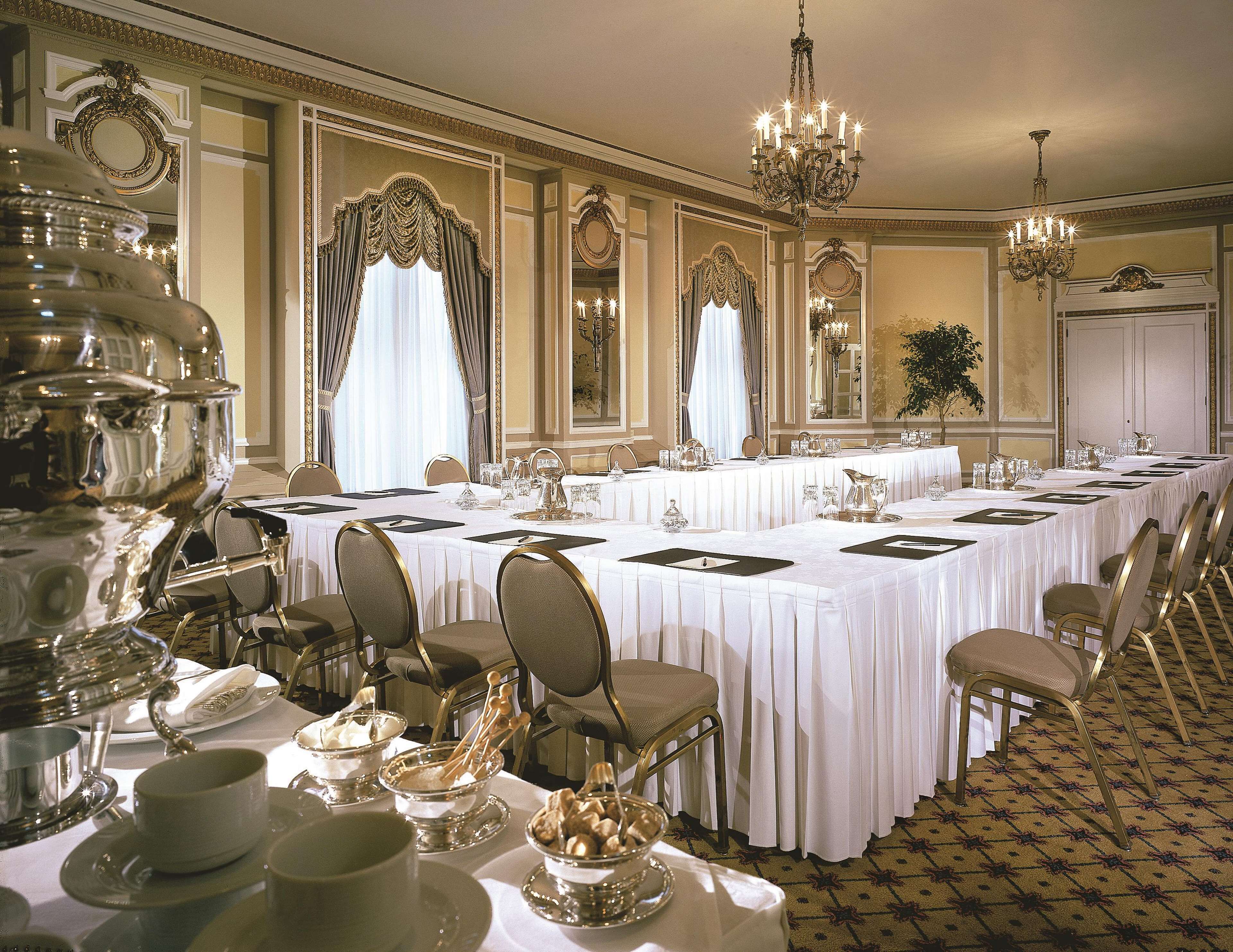 A formal dining room with a long table set for a banquet, ornate chandeliers, and classic decor.