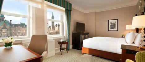 A hotel room with a bed, a desk, a chair, a TV, and a view of a cityscape through the window.