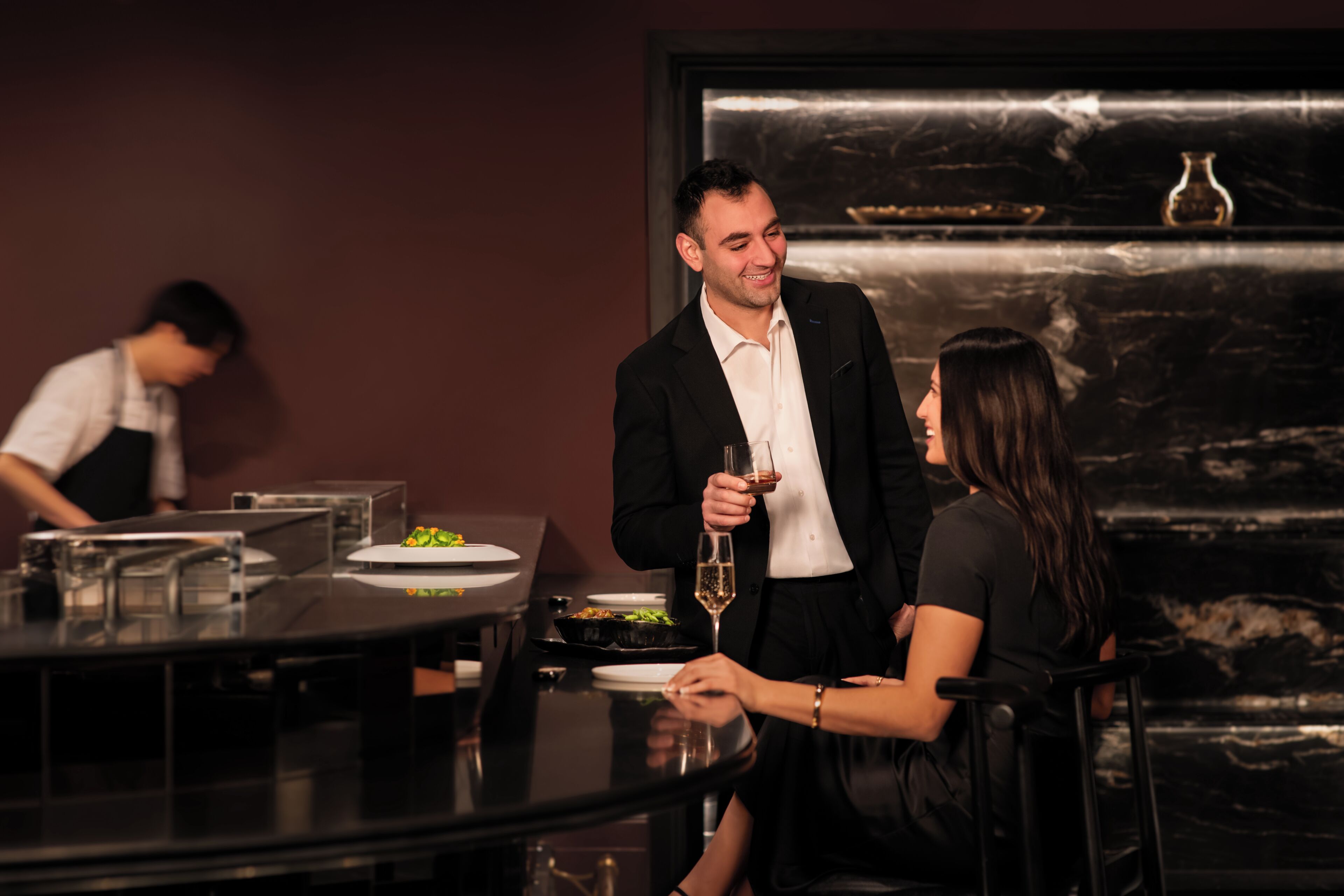 A dining area with a marble wall, a waiter, and a couple seated at a table.