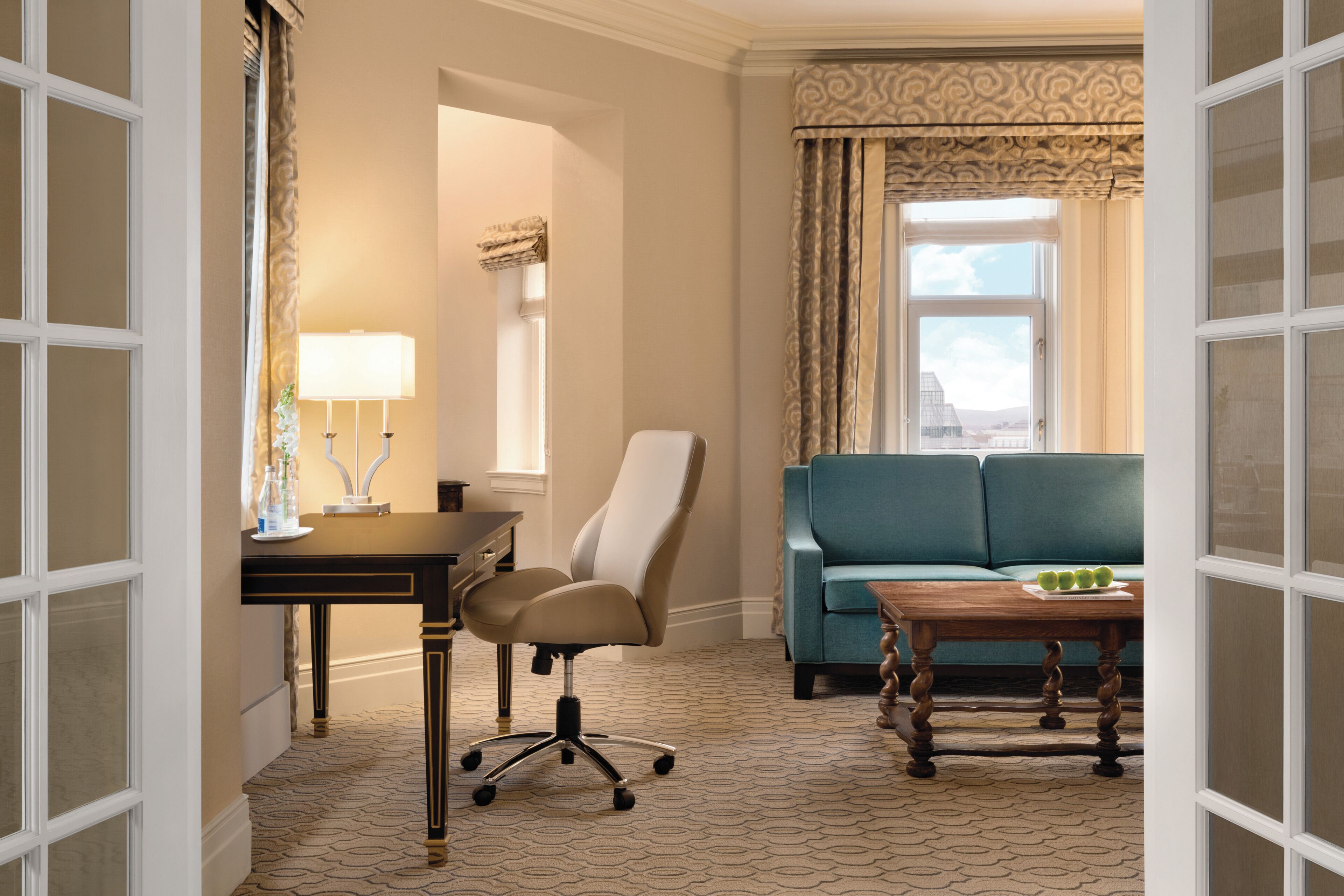 A hotel room with a desk, chair, sofa, and a small table with fruit.