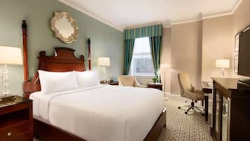 A hotel room with a large bed, two bedside tables, a desk with a chair, a mirror, and a window with curtains.