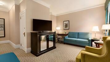 Una habitación de hotel con televisor, sofá, sillón, escritorio y lámpara.