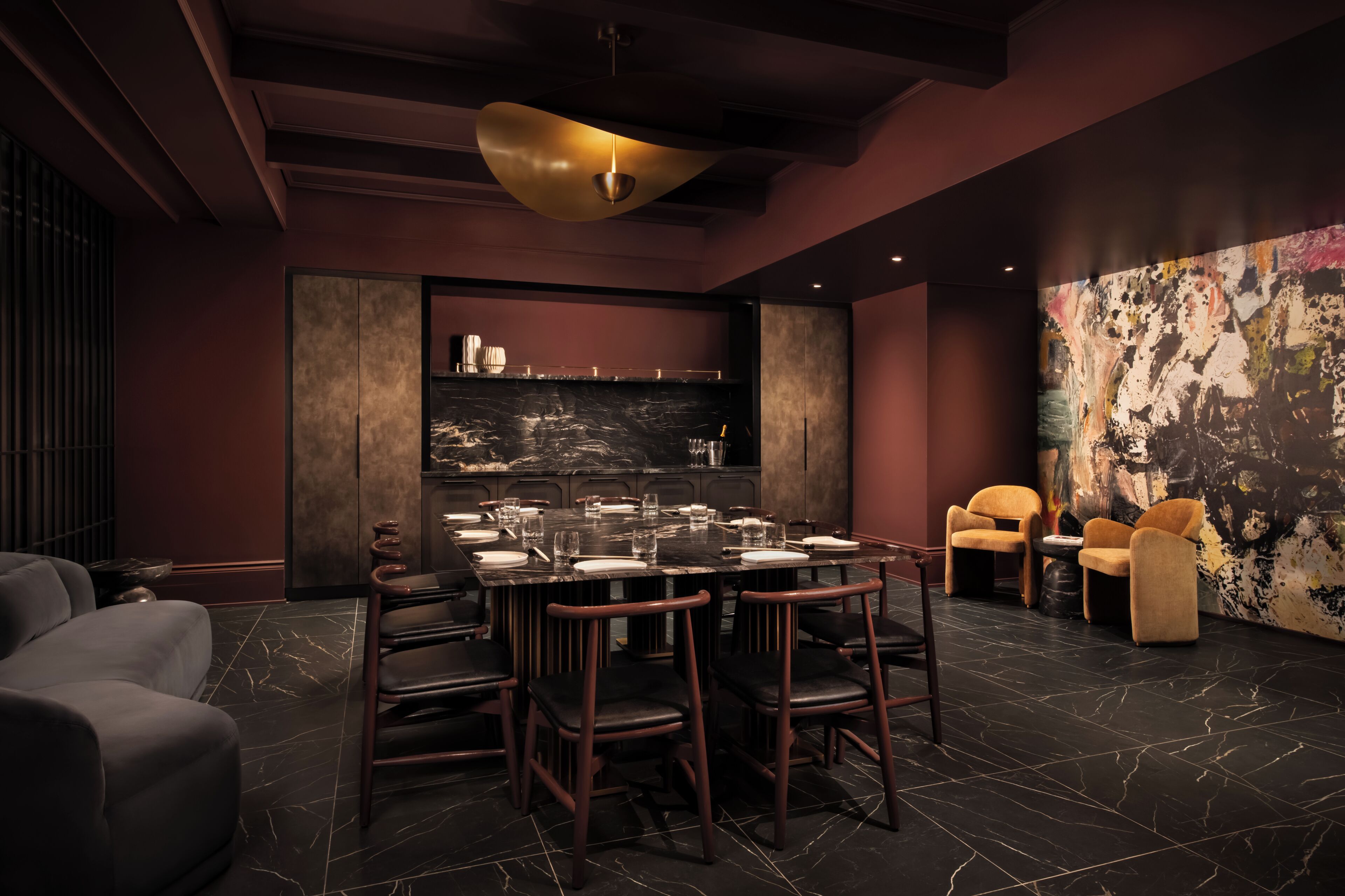 A modern dining area with a marble floor, dark furniture, and a large abstract painting on the wall.