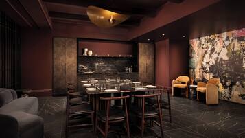 A modern dining area with a marble floor, dark furniture, and a large abstract painting on the wall.
