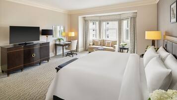 A hotel room with a large bed, a flat-screen TV, a desk with a chair, a sofa, and a window with curtains.