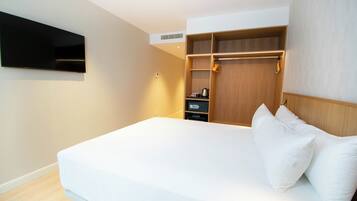 A hotel room with a bed, a TV mounted on the wall, a wardrobe, and a shelf with a kettle.