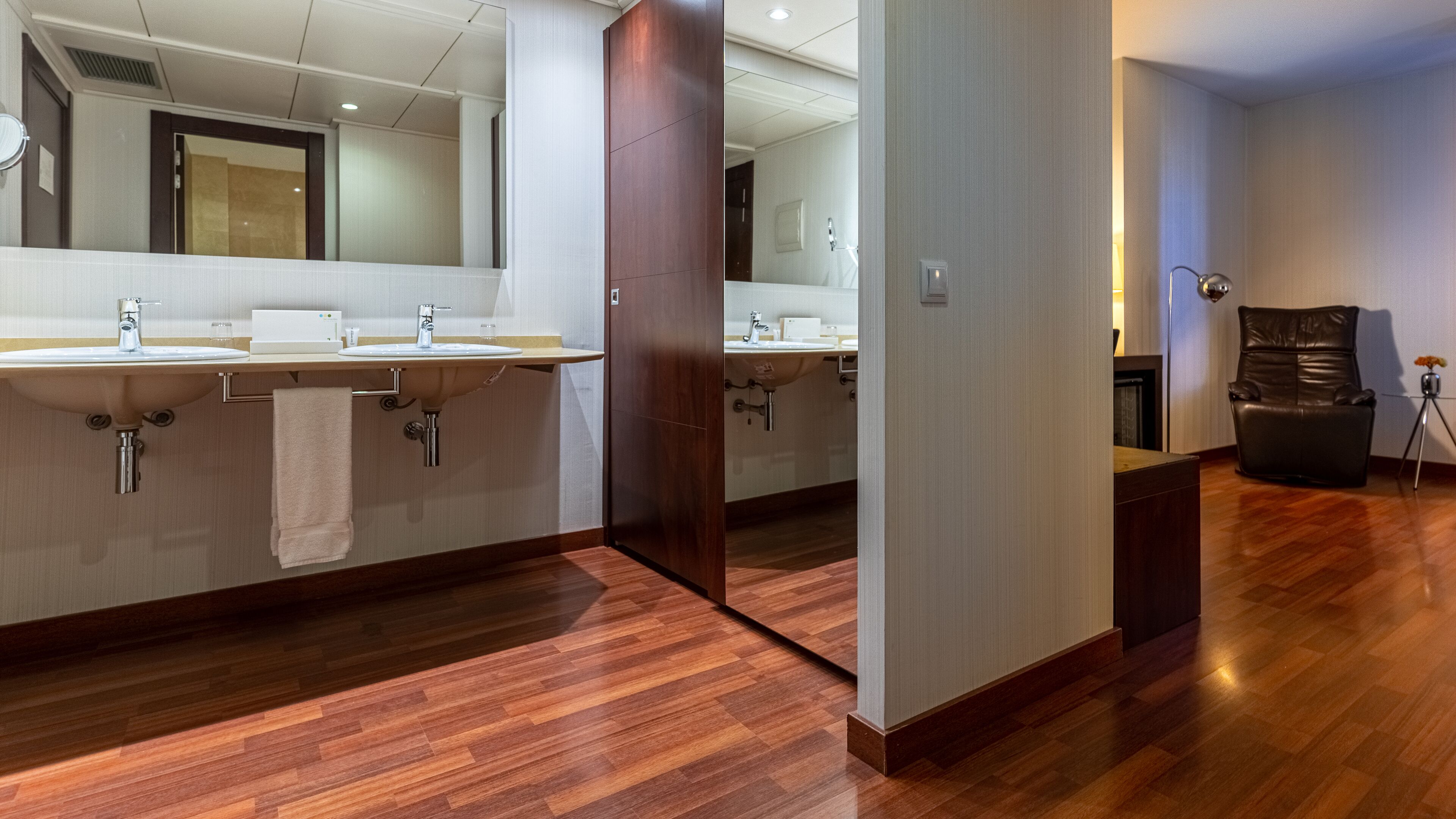 Un baño moderno con dos lavamanos, un espejo grande y suelo de madera.