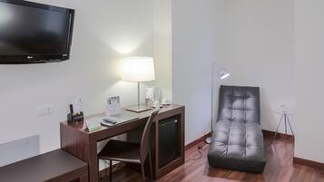 Habitación de hotel con escritorio, silla, televisor de pantalla plana, lámpara y sillón de cuero.