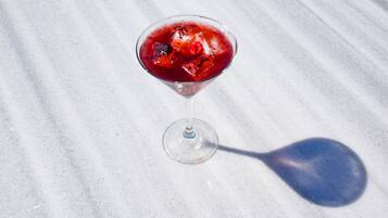 Una copa de martini con una bebida roja y cubitos de hielo sobre una superficie de mármol.