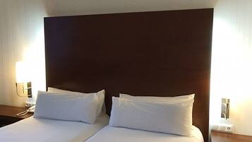 Cama doble con sábanas blancas en una habitación de hotel.