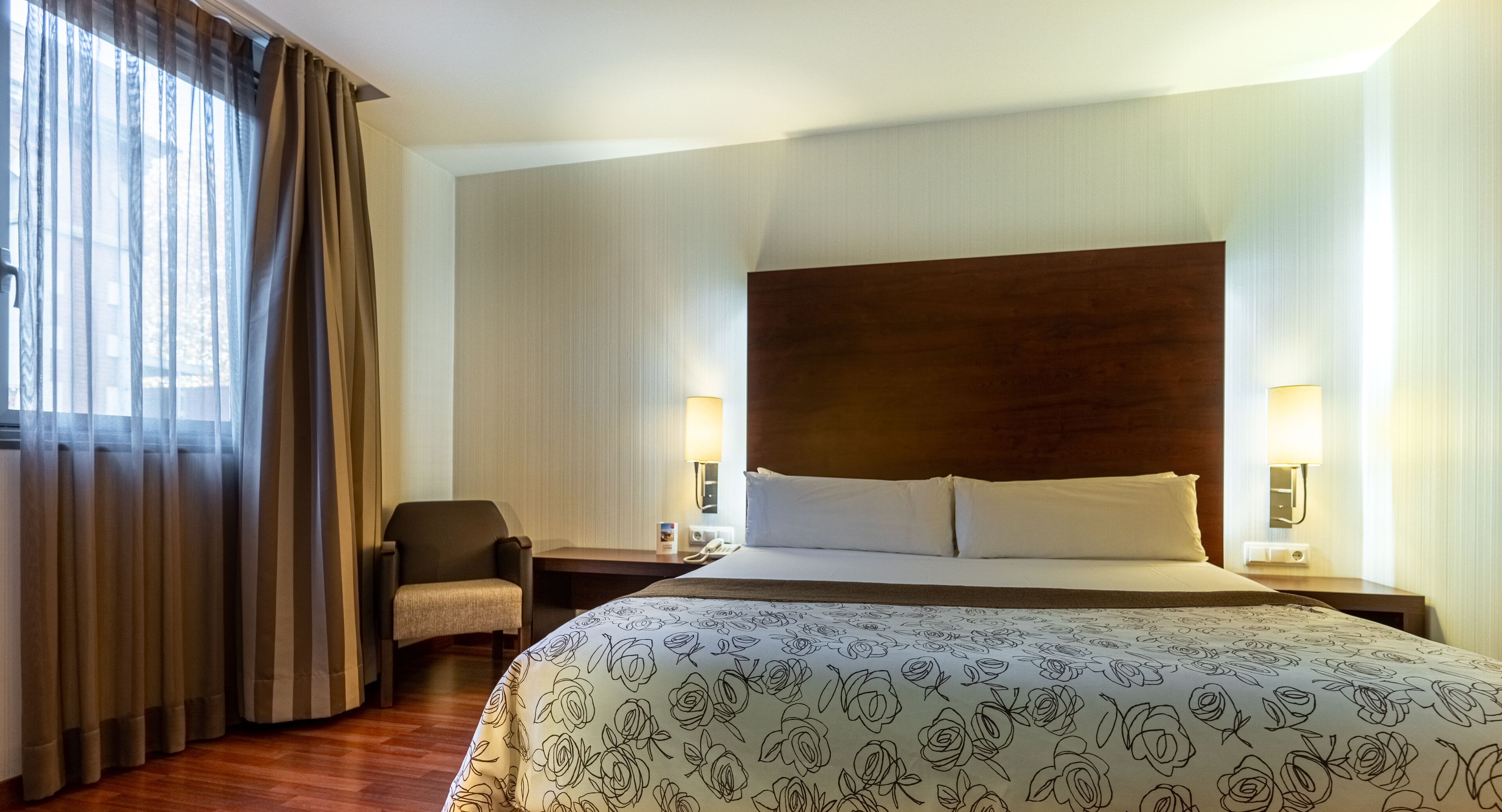 Une chambre d’hôtel avec un grand lit, une chaise, une table de chevet et une lampe.
